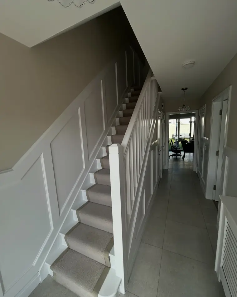 Hall and stairs with white wall panelling below a soft grey wall