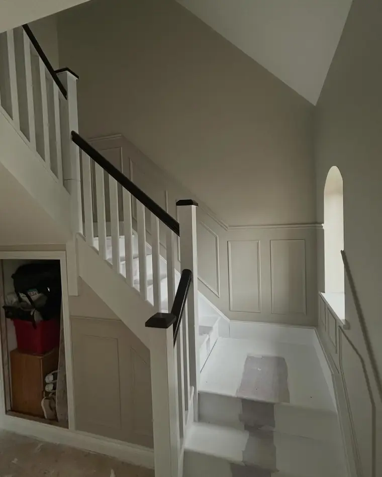 Staircase with white spindles, a panelled wall and a black handrail