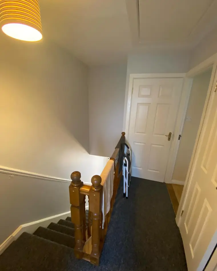 Stairs and landing in evening light with a timber handrail and white walls