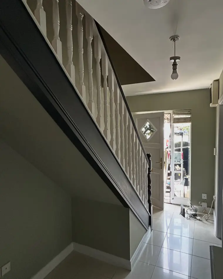 Hall and stairs with a deep sage wall, white spindles and a tiled floor